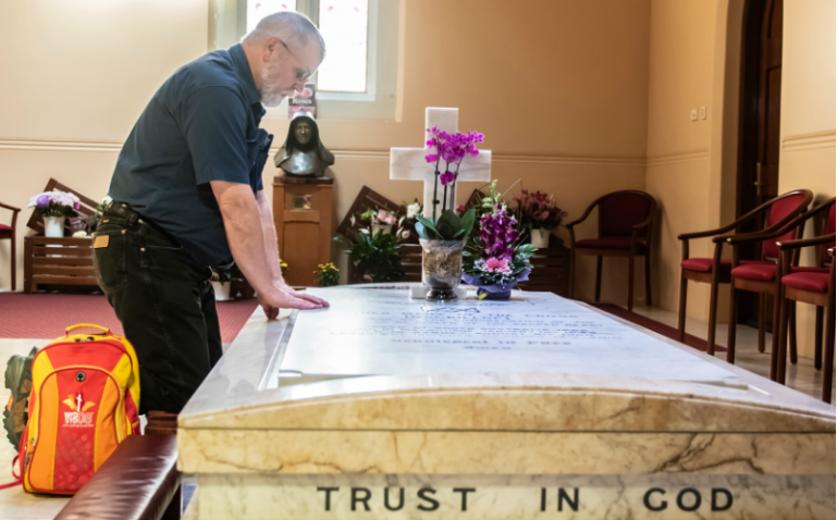 Ricky Peterson se arrodilla ante la tumba de St Mary MacKillop en el norte de Sydney con su mochila WYD08. FOTO: Giovanni Portelli / The Catholic Weekly